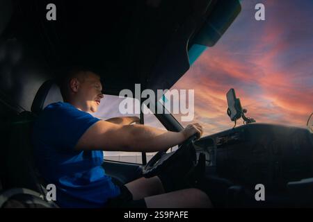 Man driving a truck at sunset with a calm expression and a smartphone holder on the windshield Stock Photo