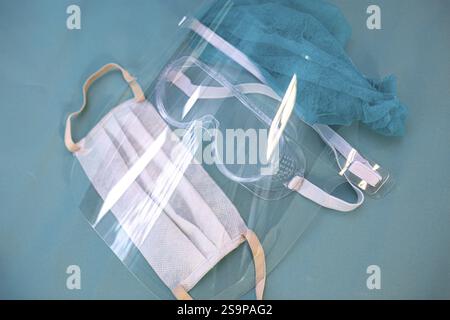 A protective set including a mask and glasses with a clear shield on a teal surface Stock Photo