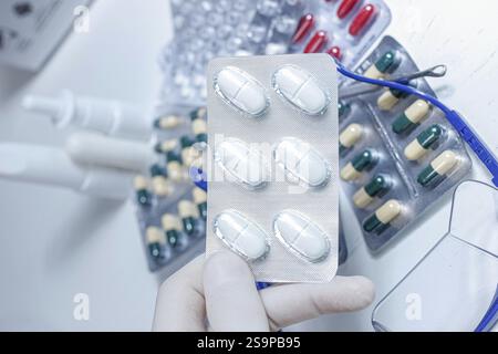 A hand in a glove holding a blister pack of white pills with capsule packs in the background Stock Photo