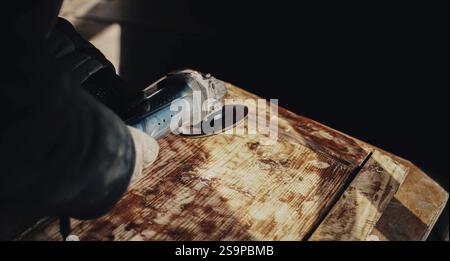 Person using an angle grinder for sanding on a textured wooden workbench Stock Photo
