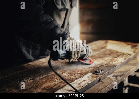 Craftsman using an angle grinder on wood, set in a rustic workshop environment Stock Photo