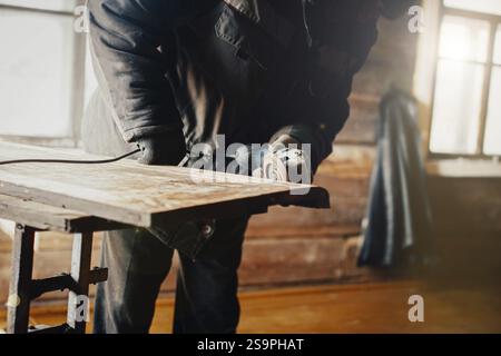 Carpenter working on a wood plank indoors, using a grinder in a workshop setting Stock Photo