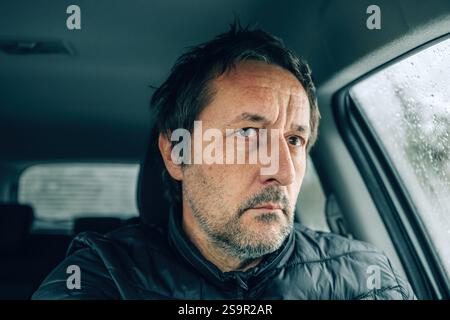 Worried male driver sitting in a car on cold winter snowy day, looking through the vehicle windscreen on icy road ahead, selective focus Stock Photo