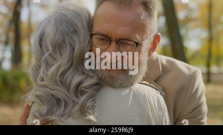 Retired senior mature old Caucasian man embracing cuddling hugging woman affection love couple in park outdoors male female affectionate bonding Stock Photo