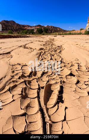 A desert landscape with a large crack in the ground. The crack is long and wide, stretching across the entire scene. The sky above is clear and blue, Stock Photo