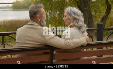 Rear back view Caucasian family happy old couple in love married husband wife senior mature retired woman man smiling talking on bench in park Stock Photo