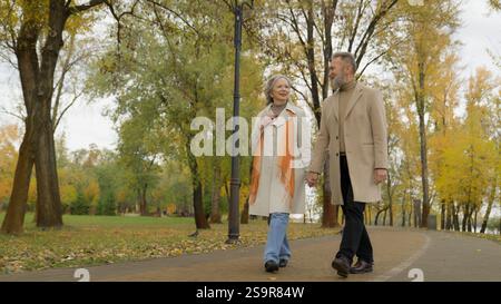 Happy old elegant couple walking in autumn park enjoying date senior man stroll with mature woman outside in city active retirement middle-aged 60s Stock Photo