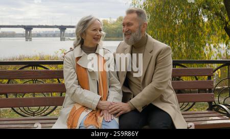 Happy senior husband and wife talking together on bench outdoors healthy elderly retirement wisdom married couple relax enjoy romantic date in city Stock Photo