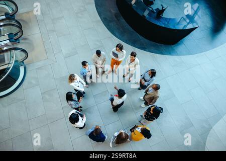 High angle view of a diverse group of professionals standing in a circular formation during an orientation session in a modern office lobby. Stock Photo