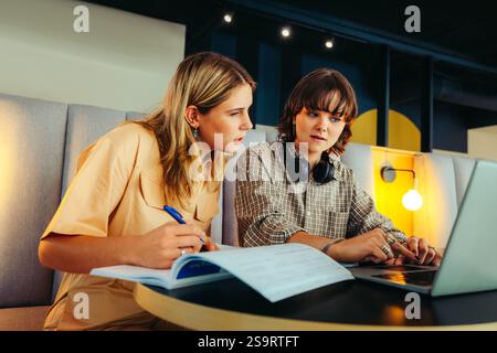 Two female students working on a project, engaging with a laptop and textbooks in a collaborative study environment. Stock Photo