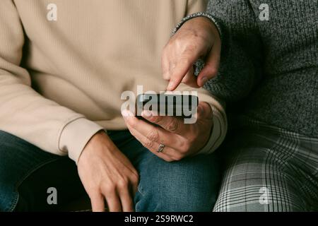 closeup of two men wearing casual clothes, sitting side by side on a brown sofa, and one of them shows something in his smartphone to his partner Stock Photo
