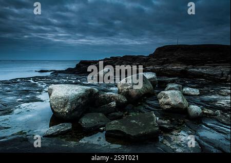 Biskopshagen nature reserve features rugged coastal rocks emerging from tidal waters as the twilight sky turns gray, enhancing the serene atmosphere o Stock Photo