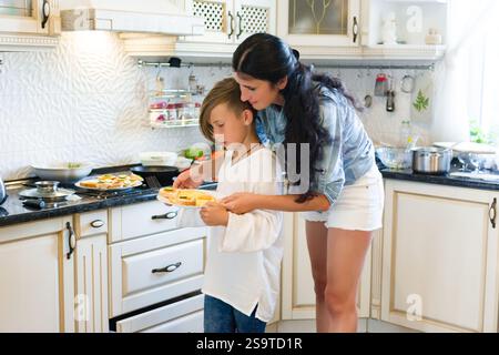 A heartwarming scene of a mother and son bonding in the kitchen. They're collaboratively preparing food, showing teamwork and care. The kitchen is bri Stock Photo