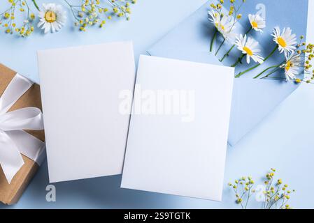 Greeting or invitation card mockup, two white empty blanks  with floral decor on bue background, copy space. Stylish creative mockup with white chamom Stock Photo