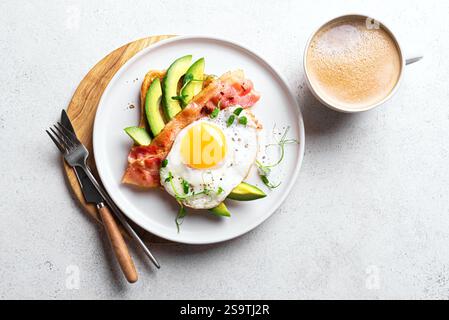 Breakfast sandwich with fried egg, bacon, avocado and microgreens on white background, top view, copy space. Organic egg with bacon on toast and morni Stock Photo