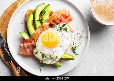 Toasted sandwich with fried egg, bacon, avocado and microgreens for healthy breakfast. Homemade breakfast keto toast and coffee close up. Stock Photo