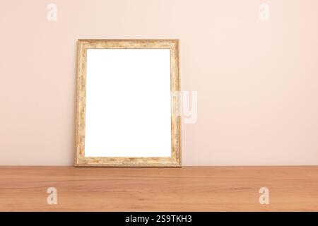 Blank frame mockup on a wooden desk in front of beige wall. Place for text. Stock Photo