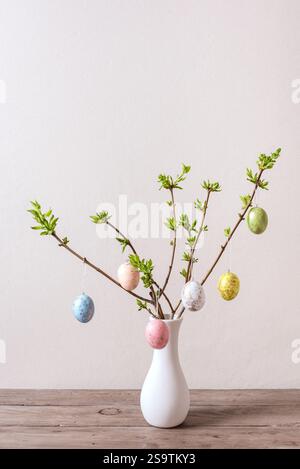 Vase with colorful Easter eggs hanging on spring branches, neutral background, minimal composition. Happy Easter concept. Stock Photo