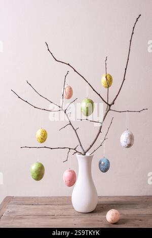 Painted Easter eggs on twigs in white vase, neutral background, minimal composition. Happy Easter decor. Stock Photo