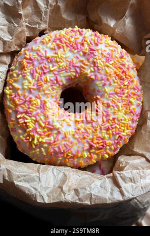 Iced ring doughnuts sprinkled with hundreds and thousands in a brown paper bag. Recycling eco friendly biodegradable packaging Stock Photo