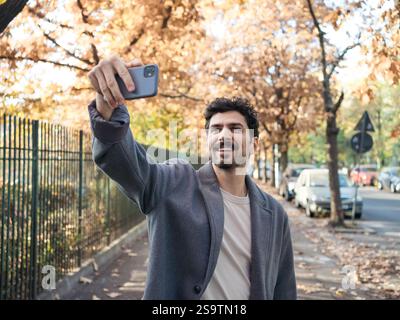 Closeup portrait of young smiling middle eastern man taking selfie with phone on a beautiful autumn day. Stock Photo