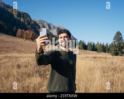 Handsome man taking selfies with beautiful landscape of the mountains behind him - Traveling and technology. Autumn season. Stock Photo