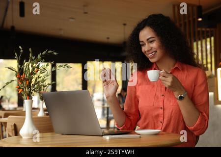 Woman with cup of coffee having video call in cafe Stock Photo