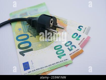Electric power adapter cord charger lies on a stack of money. Euro cash banknotes. The concept of increasing prices for electricity. Stock Photo