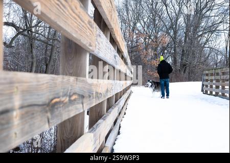 Man walking a malamute dog across a bridge that is covered in snow Stock Photo