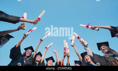 Smiling graduates joyfully raising diplomas to the sky, celebrating their hard earned achievements on graduation day Stock Photo