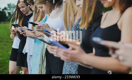 Teenagers in a line outdoors during summer, using smartphones to connect and communicate Stock Photo