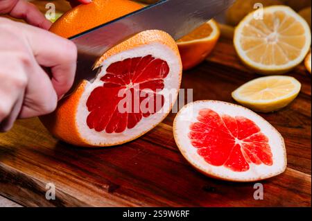 Person slicing a grapefruit on a wood cutting board Stock Photo