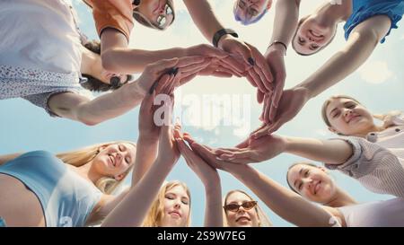 Friends at school joining hands in a circle, representing unity, teamwork, and friendship under a clear blue sky Stock Photo