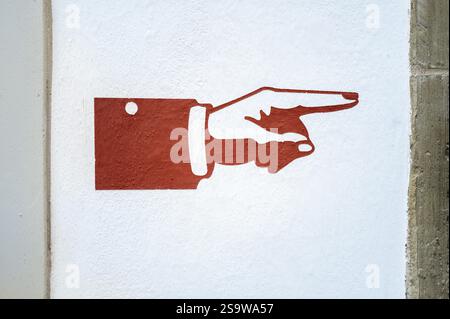 A reddish-brown hand pointing right is painted on a white wall. The simple design serves as a clear directional indicator. The wall texture is visible Stock Photo