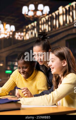 Two preteens scholars and their tutor collaborating on schoolwork at the library, focused on academic success and learning development. Students collect extra information with private lessons. Stock Photo