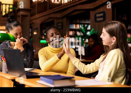 Satisfied teenagers students doing high five next to tutor in the library, feeling happy with their progress on school subjects. Professor being proud of her scholars at private lessons. Stock Photo