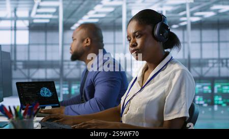 Data center engineer wearing headphones enjoying songs, maintaining company network infrastructure. Woman in server hub listening music while ensuring optimal system performance, camera A Stock Photo