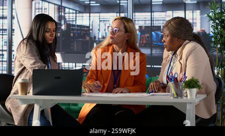 Diverse business experts sharing ideas for corporate growth planning, analyzing infographics for monthly report task. Powerful women working together to ensure organizational productivity. Camera A. Stock Photo