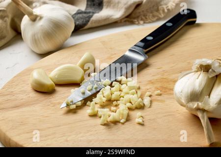 fresh raw garlic and knife on kitchen table on wooden cutting board. Process of making french onion soup, food closeup, cutting garlic for healthy mea Stock Photo