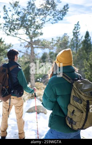 Young unrecognizable couple in a snowy mountain admiring the forest landscape. Stock Photo