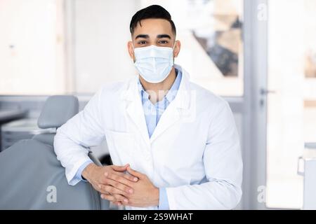 Portrait Of Young Middle Eastern Dentist Wearing Protective Medical Mask Posing At Workplace Stock Photo
