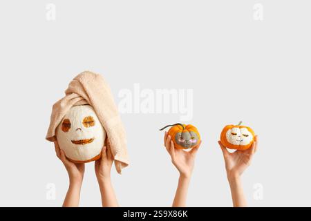 Female hands holding pumpkins with drawn faces and clay masks on white background Stock Photo