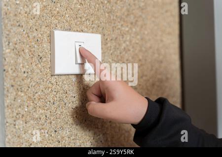 Woman hand pushing light switch at home. A woman turns off the home light switch when she leaves the room. Power, energy saving, energy saving. Hand t Stock Photo