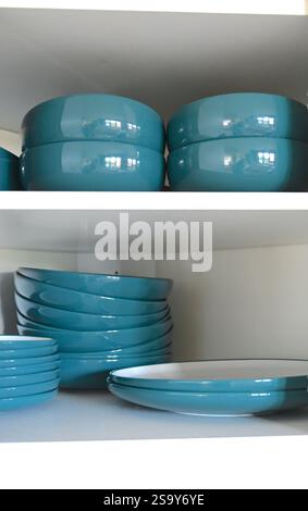 Teal plates on white shelves in kitchen cabinet, vertical shot. Stock Photo