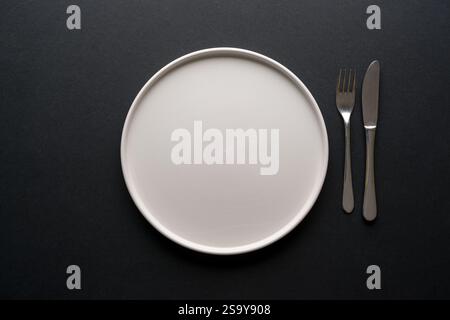 Top view of empty ceramic white plate and cutlery on black background Stock Photo