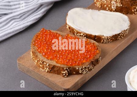 Freshly prepared rye bread topped with vibrant salmon roe and creamy spread on a wooden board Stock Photo