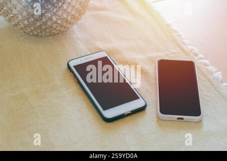 Two mobile phones on the dining room table with a tablecloth near by glass vase. Smartphone concept. Stock Photo