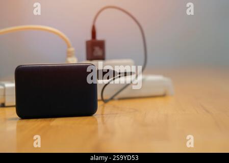Extension cord with charging gadgets on wooden table at home. Close up, selective focus. Stock Photo