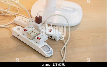 Messy outlet power extension cord on an apartment floor with various charging devices plugged Stock Photo