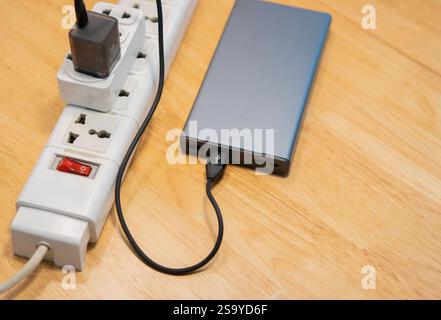 Top view of the power bank is charging with multiple socket on wooden desk. Selective focus. Stock Photo